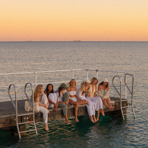 Group of women sitting on a dock by the water at sunset
