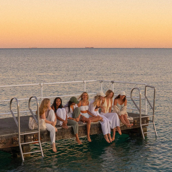 Group of women sitting on a dock by the water at sunset